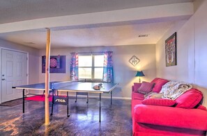 A ping pong table in a room with a red couch, a dartboard, and a wall clock. - Large Cabin w/ Deck Overlooking Norfork Lake! (Elizabeth)