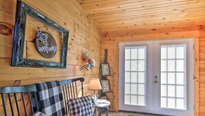 A wooden interior with a checkered sofa, a welcome sign, a lamp, and a framed picture on the wall.