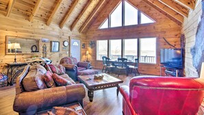 A cozy log cabin interior with a high ceiling, wooden walls, a fireplace, a television, and a dining area.
