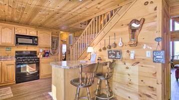 Een houten interieur met een keukenhoek, een bar met krukken en een trap.