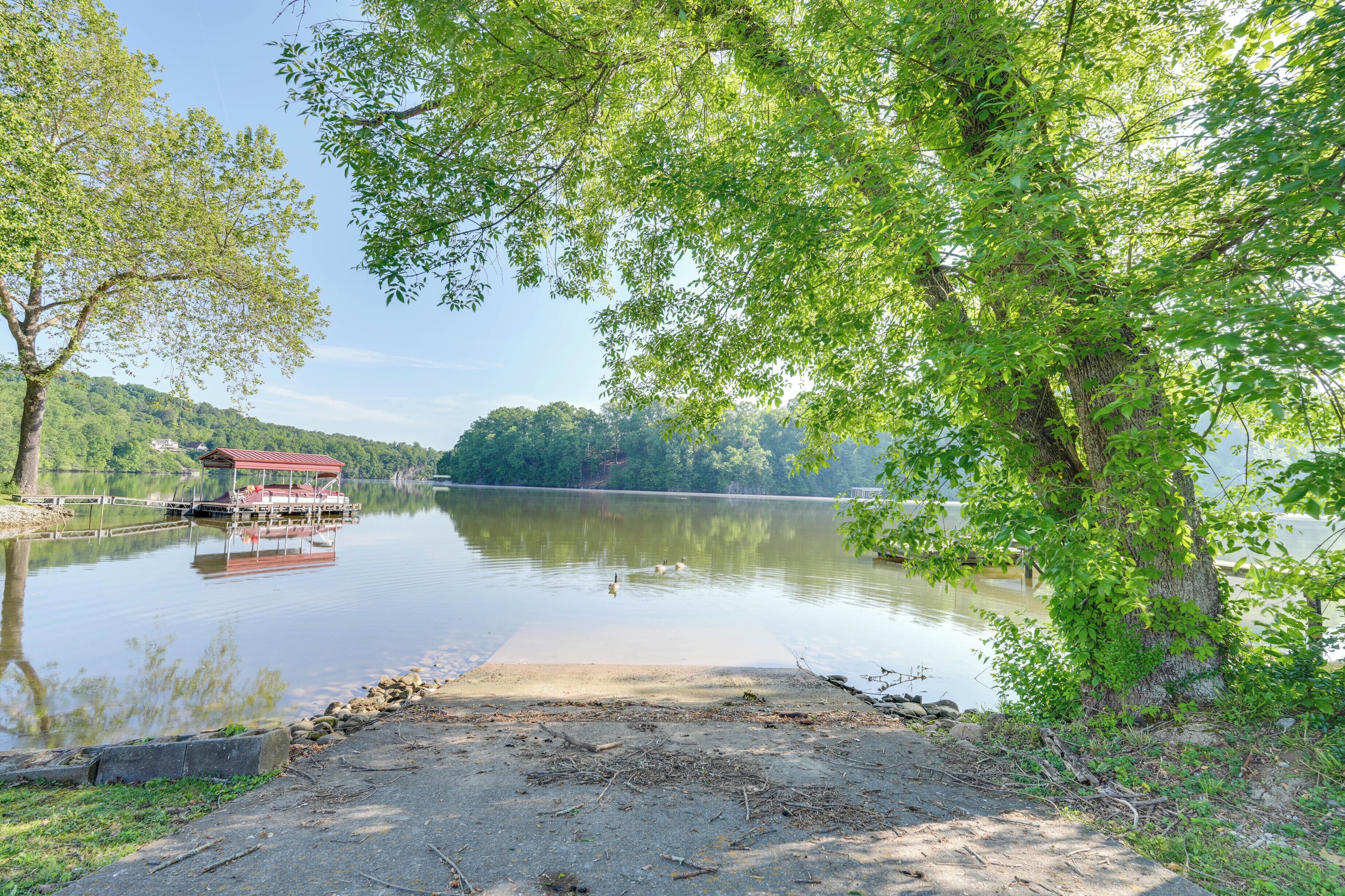 A lakeside dock with a red building, calm water, and surrounding greenery.