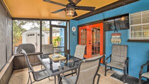 A covered patio with a glass table and chairs, a ceiling fan, and a red door. - Tropical Palm Harbor Retreat With Lanai & Patio! (Palm Harbor)