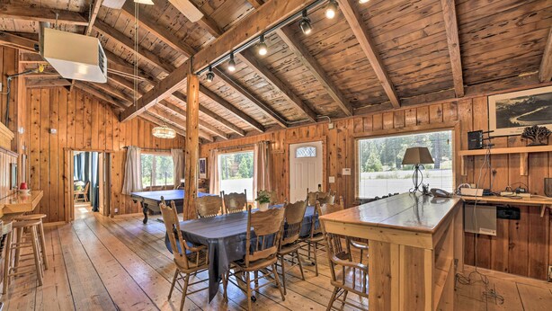 A rustic wooden interior with a dining area, kitchen, and large windows. - Secluded Camp Connell Home w/ Deck + Fireplace! (Arnold)