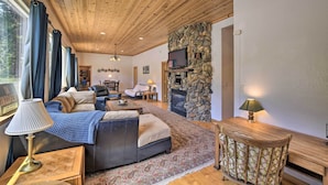 A cozy living room with a stone fireplace, wooden ceiling, and a comfortable seating area with a couch and a coffee table. - Secluded Camp Connell Home w/ Deck + Fireplace! (Arnold)