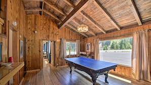 A wooden room with a ping pong table, wooden floors, and large windows with curtains. - Secluded Camp Connell Home w/ Deck + Fireplace! (Arnold)
