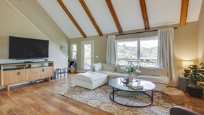 A spacious living room with a large flat-screen TV, a wooden ceiling, a sofa, a coffee table, and a view of the outdoors. - Hot Tub + Balcony: Rainbow Retreat Near Wineries! (Fallbrook)