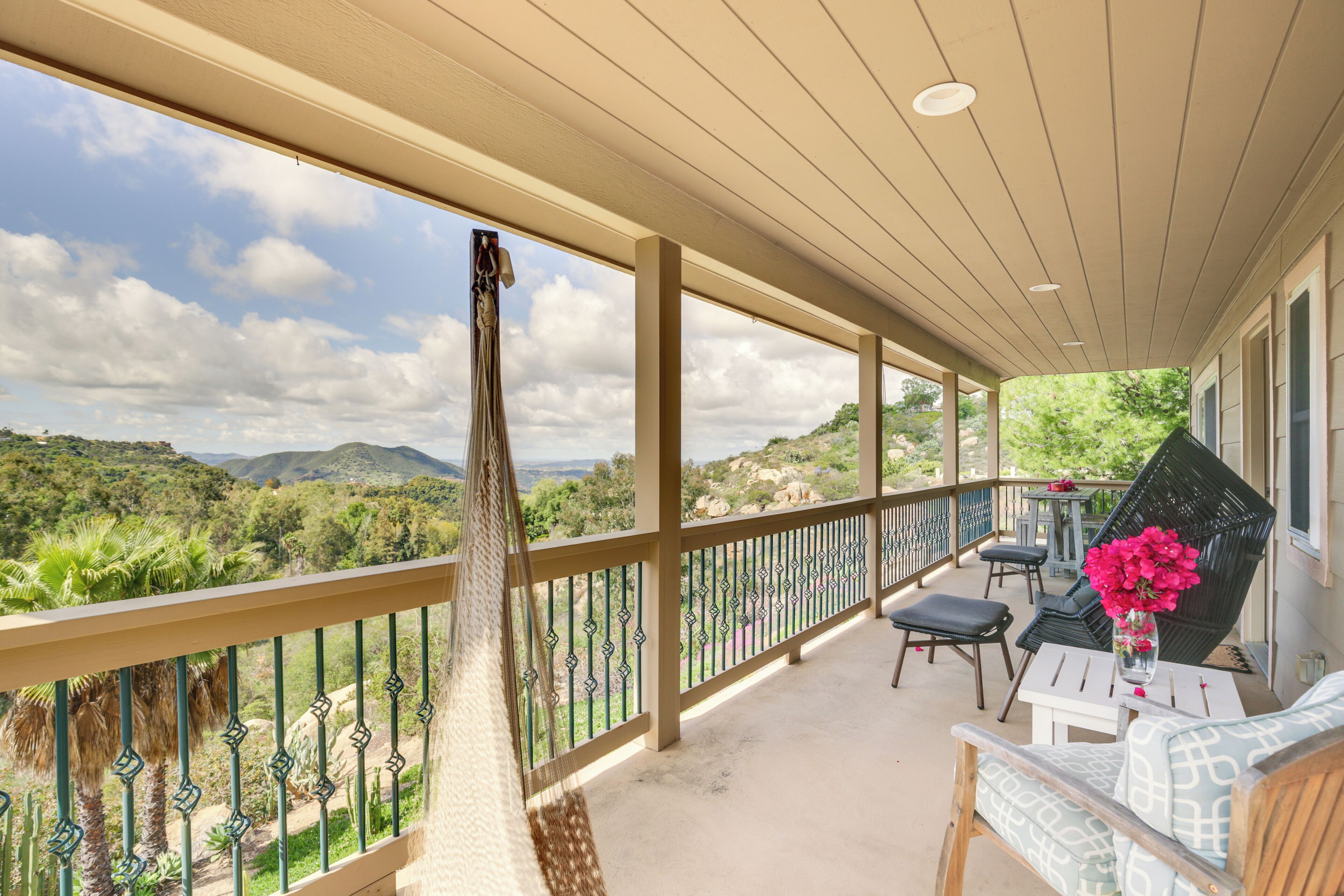 A covered balcony with a hammock, outdoor seating, and a view of the landscape.