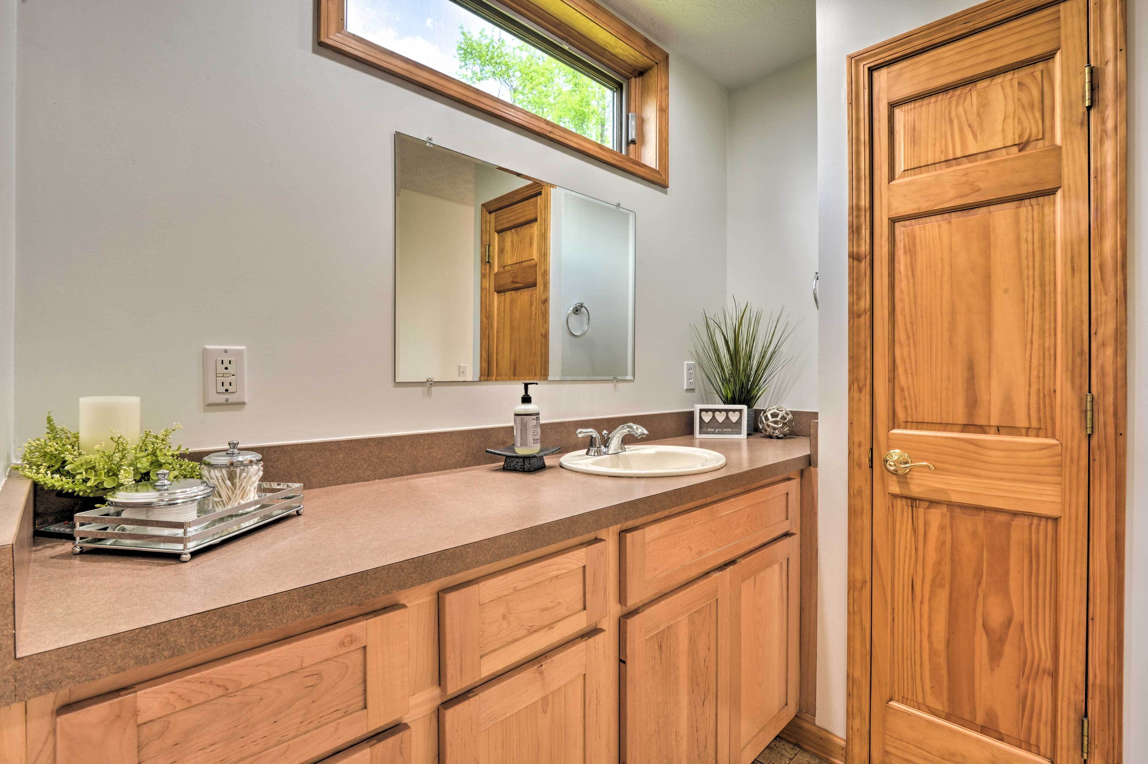 A bathroom with a wooden vanity, a sink, a mirror, and a window above the mirror.
