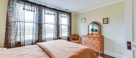 A bedroom with a large bed, a dresser, a chair, and a window with curtains.