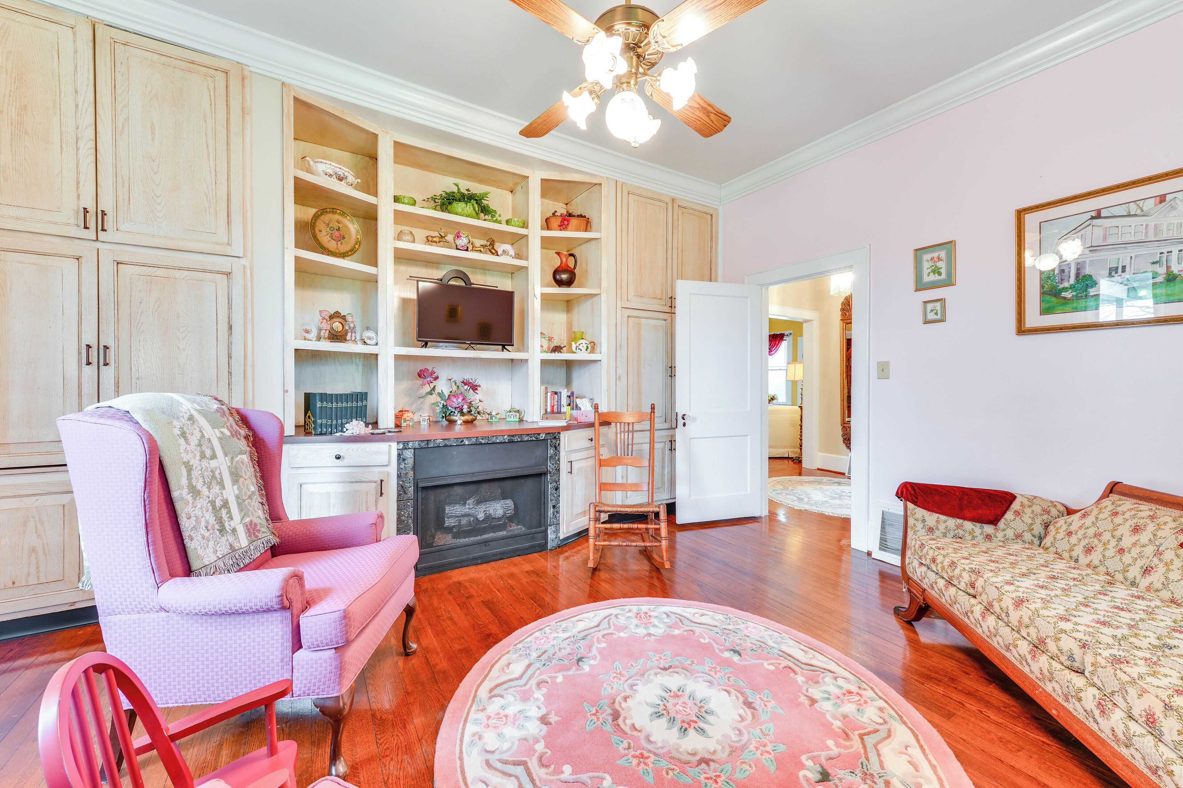 A living room with a fireplace, a pink armchair, a sofa, and a wooden floor.