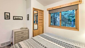 Une chambre à coucher avec un lit, une commode, une fenêtre donnant sur des arbres et des tableaux encadrés accrochés au mur.