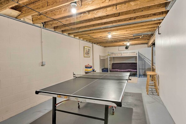 A ping pong table in a room with exposed wooden beams, white brick walls, and a bunk bed in the background. - Charming Thompsonville Home w/ On-site River! (Thompsonville)