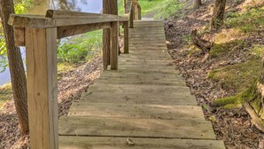Une promenade en bois menant à un pont qui enjambe une étendue d’eau, le tout étant entouré d’arbres et de verdure.