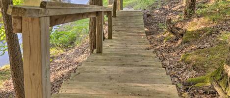 A wooden boardwalk leading to a bridge over a body of water, surrounded by trees and greenery.