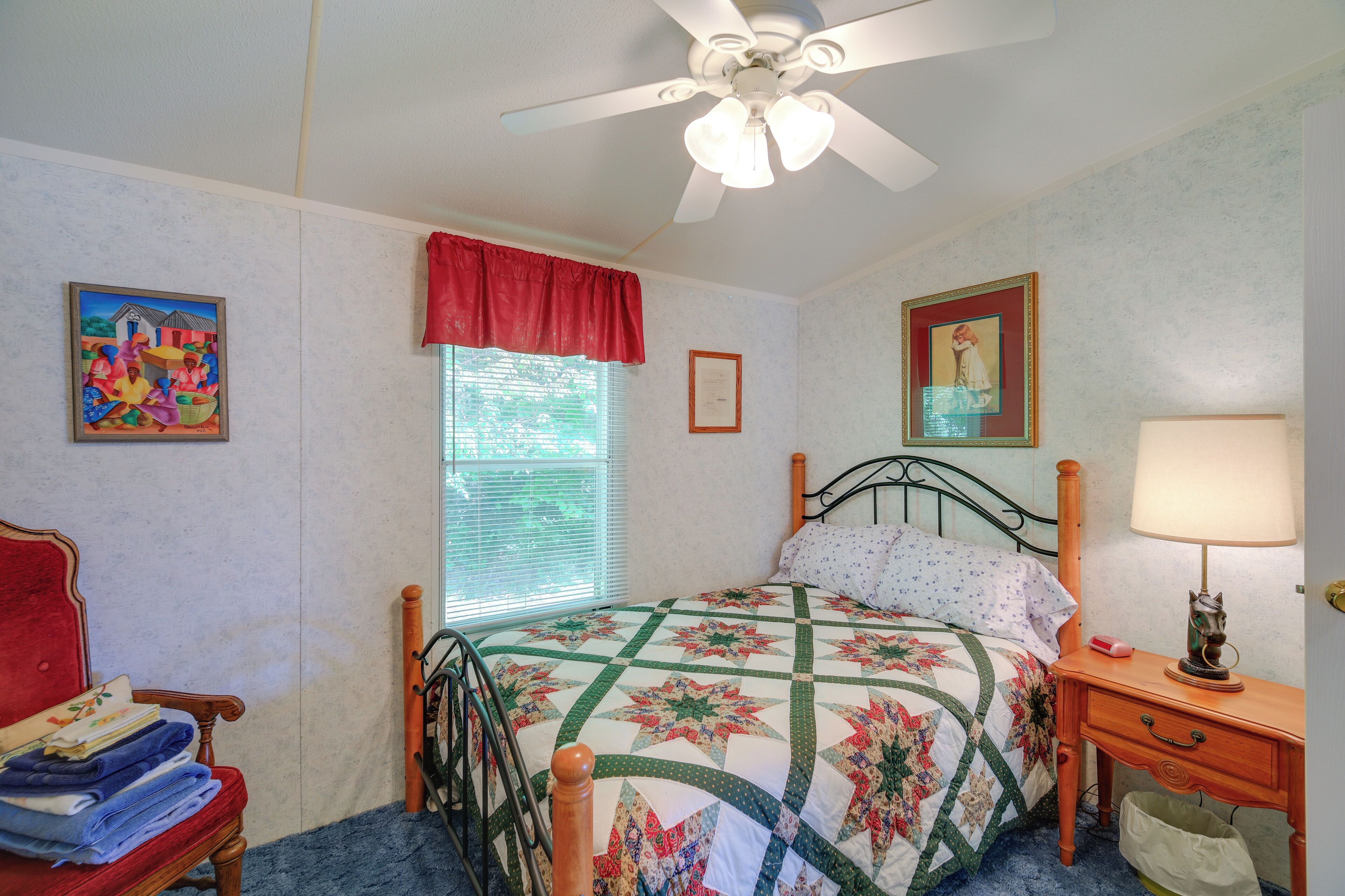 A bedroom with a bed, a nightstand, a chair, a window with blinds, and a ceiling fan.
