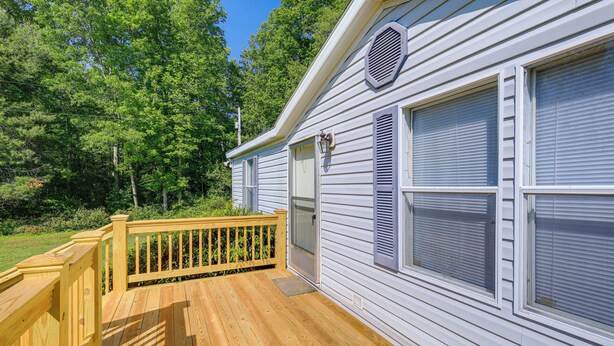 A wooden deck with a railing, a white building with shutters, and a door.