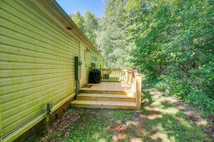 A wooden deck leading to a house with a porch, surrounded by dense greenery.