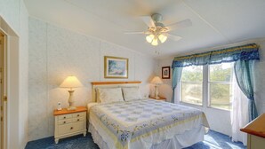 A bedroom with a bed, two bedside tables, a ceiling fan, a window with curtains, and a painting on the wall.