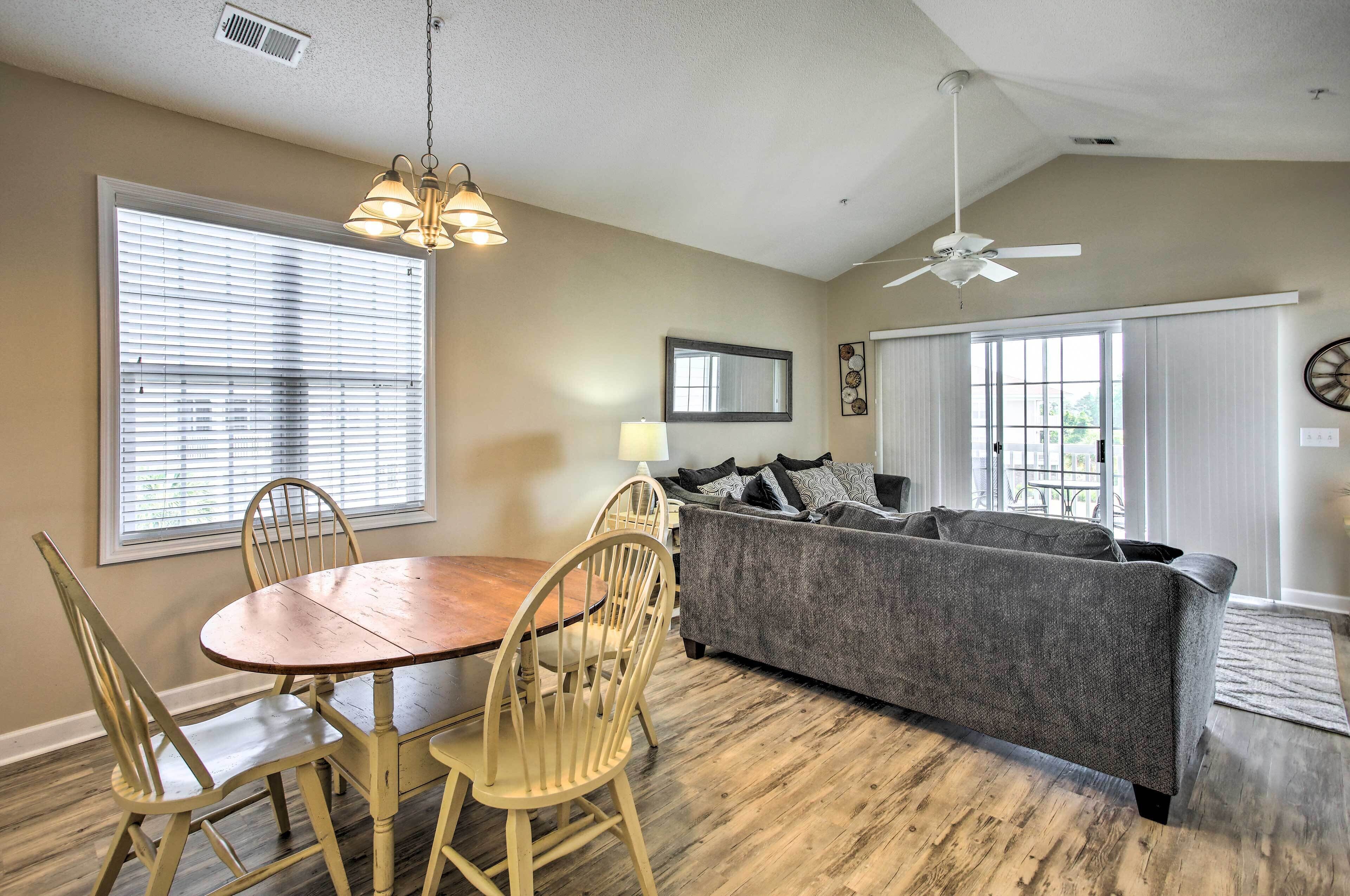 A dining area with a wooden table and chairs, a gray sofa, and a ceiling fan.