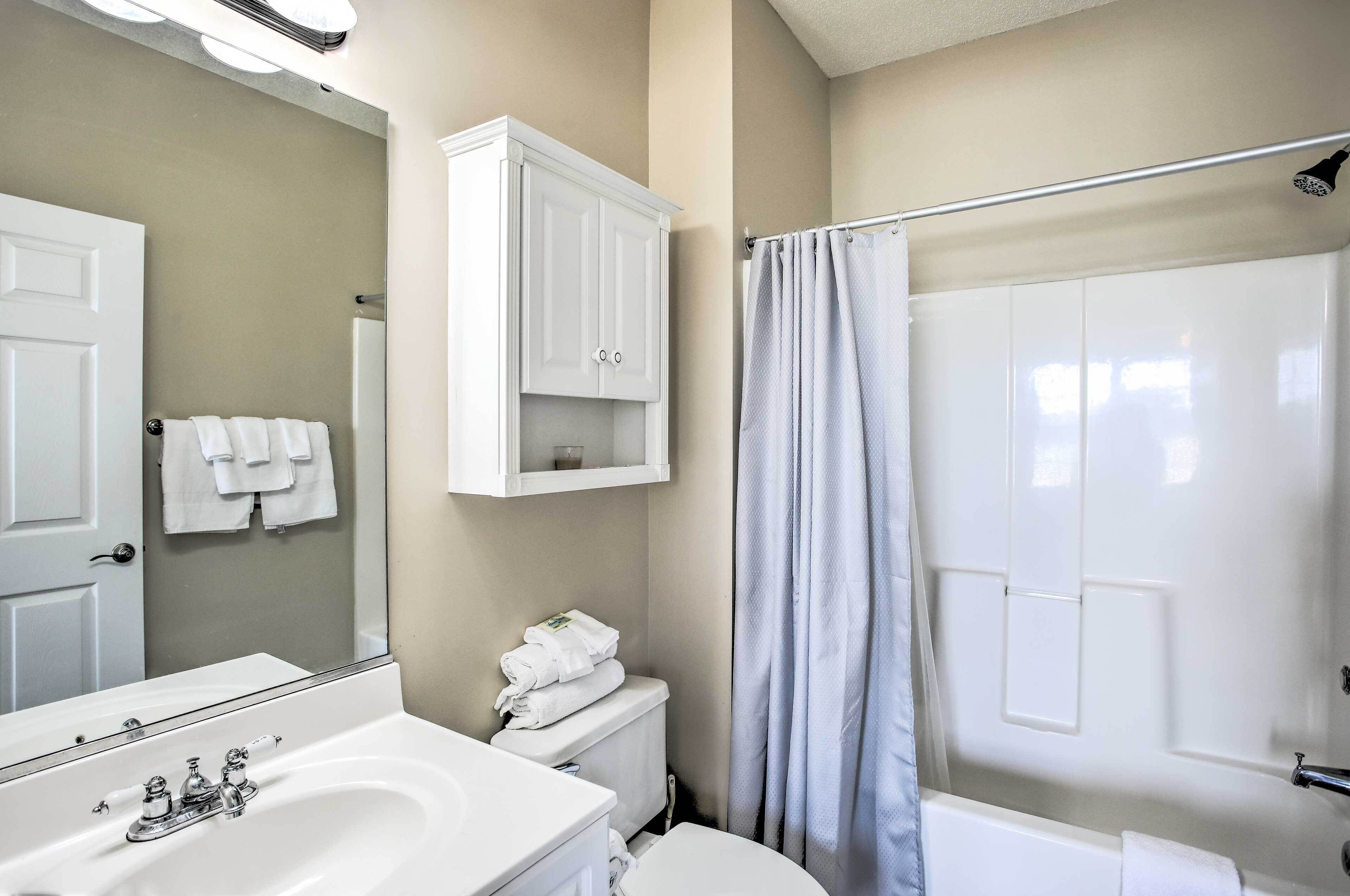 A bathroom with a white sink, mirror, cabinet, toilet, and shower curtain.
