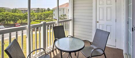 A balcony with a glass table and chairs, a white door, and a view of a residential area.