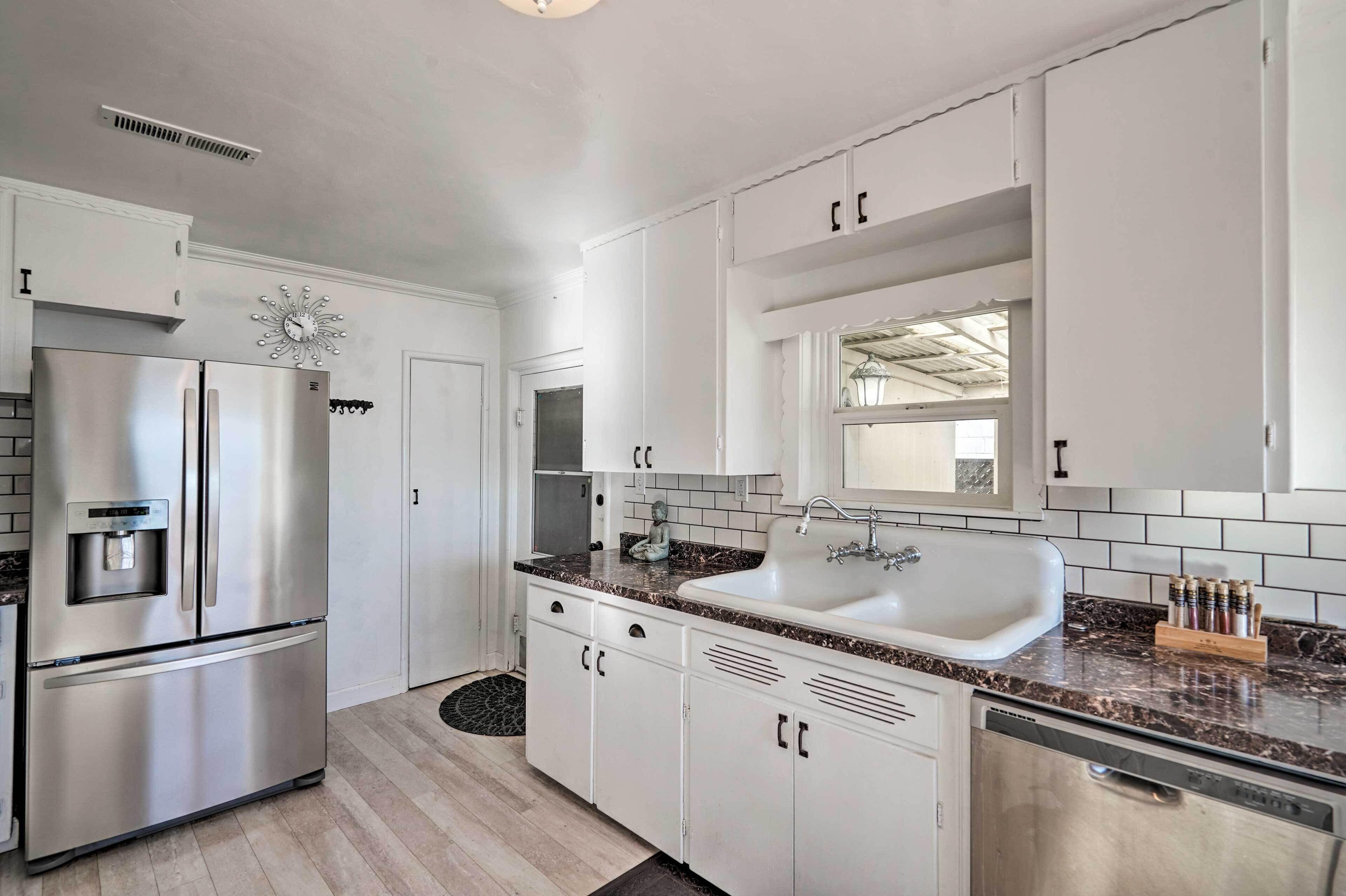 A modern kitchen with white cabinetry, a stainless steel refrigerator, a sink, and a marble countertop.