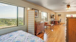 Une chambre avec un grand lit, une commode en bois, un bureau et une chaise, une vue sur l’extérieur et un ventilateur de plafond.
