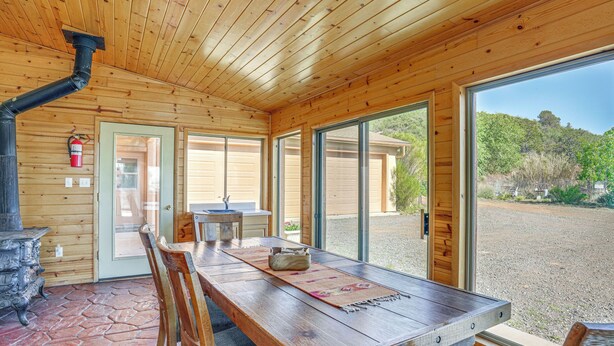 Un intérieur en bois avec un sol en pierre, une table à manger, des chaises, une cheminée et de grandes fenêtres donnant sur l’extérieur.