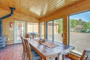 A wooden interior with a stone floor, a dining table, chairs, a fireplace, and large windows offering a view of the outdoors. - Sunroom + Sauna! Mtn-view Prescott Valley Home (Dewey)
