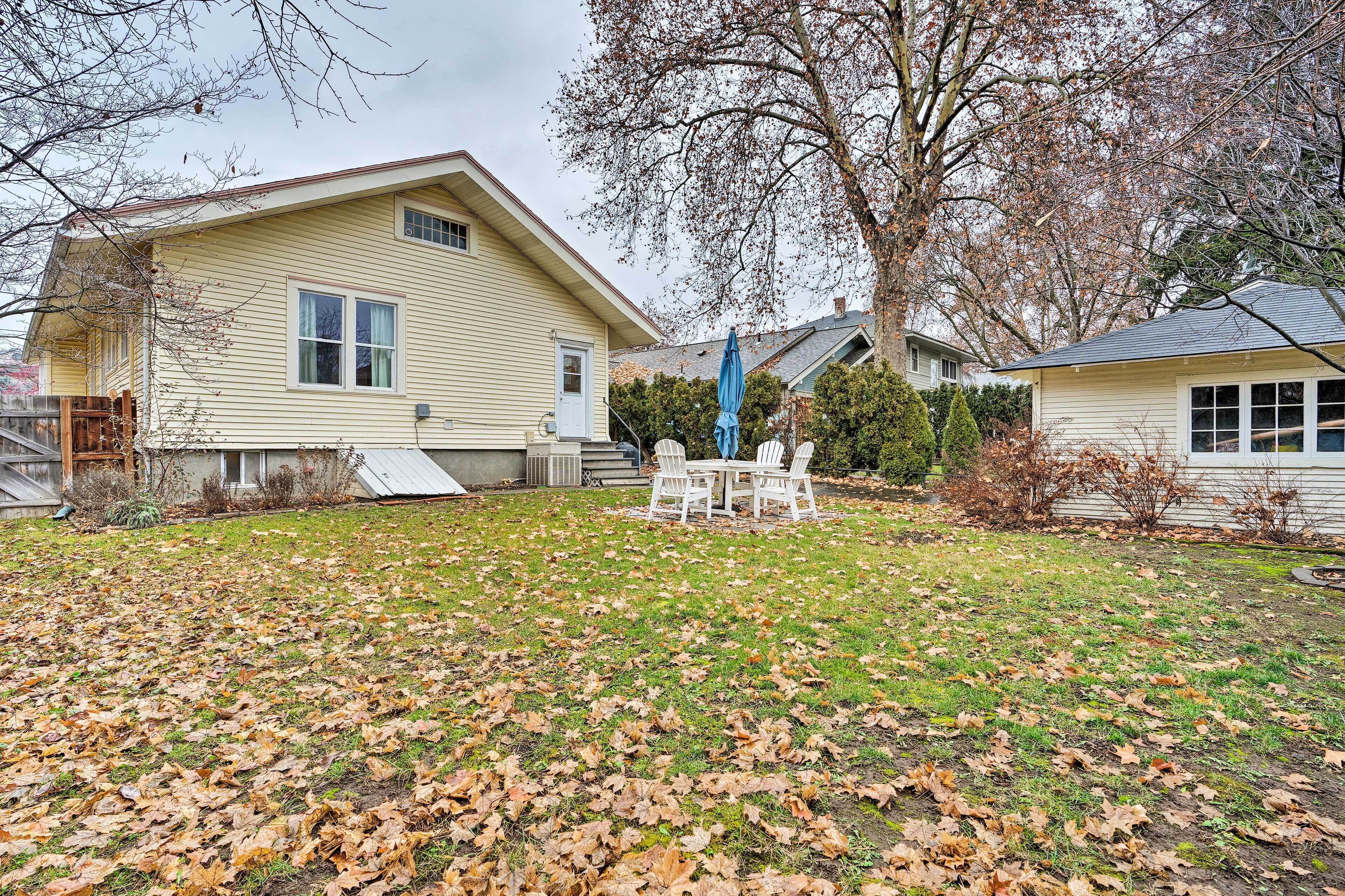 A house with a covered patio area, a lawn with scattered leaves, and a large tree in the background.