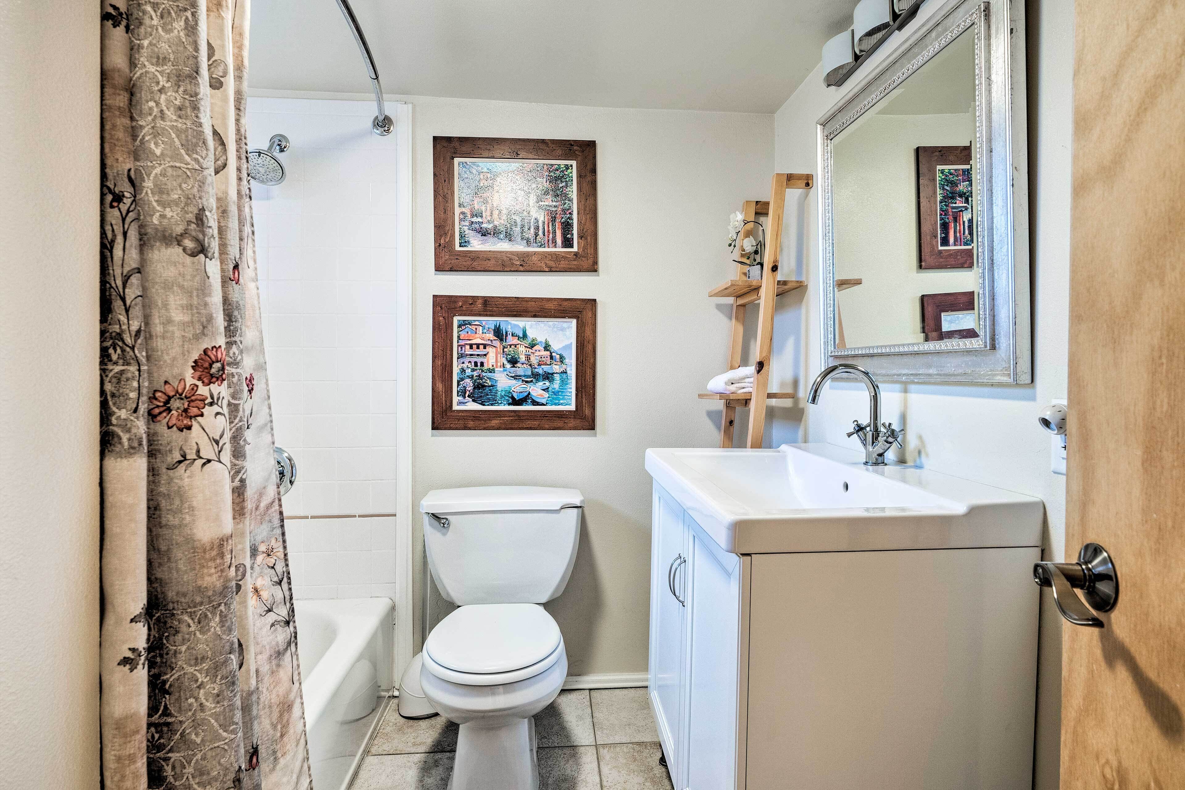 Un baño con inodoro, ducha, lavabo y dos cuadros en la pared.