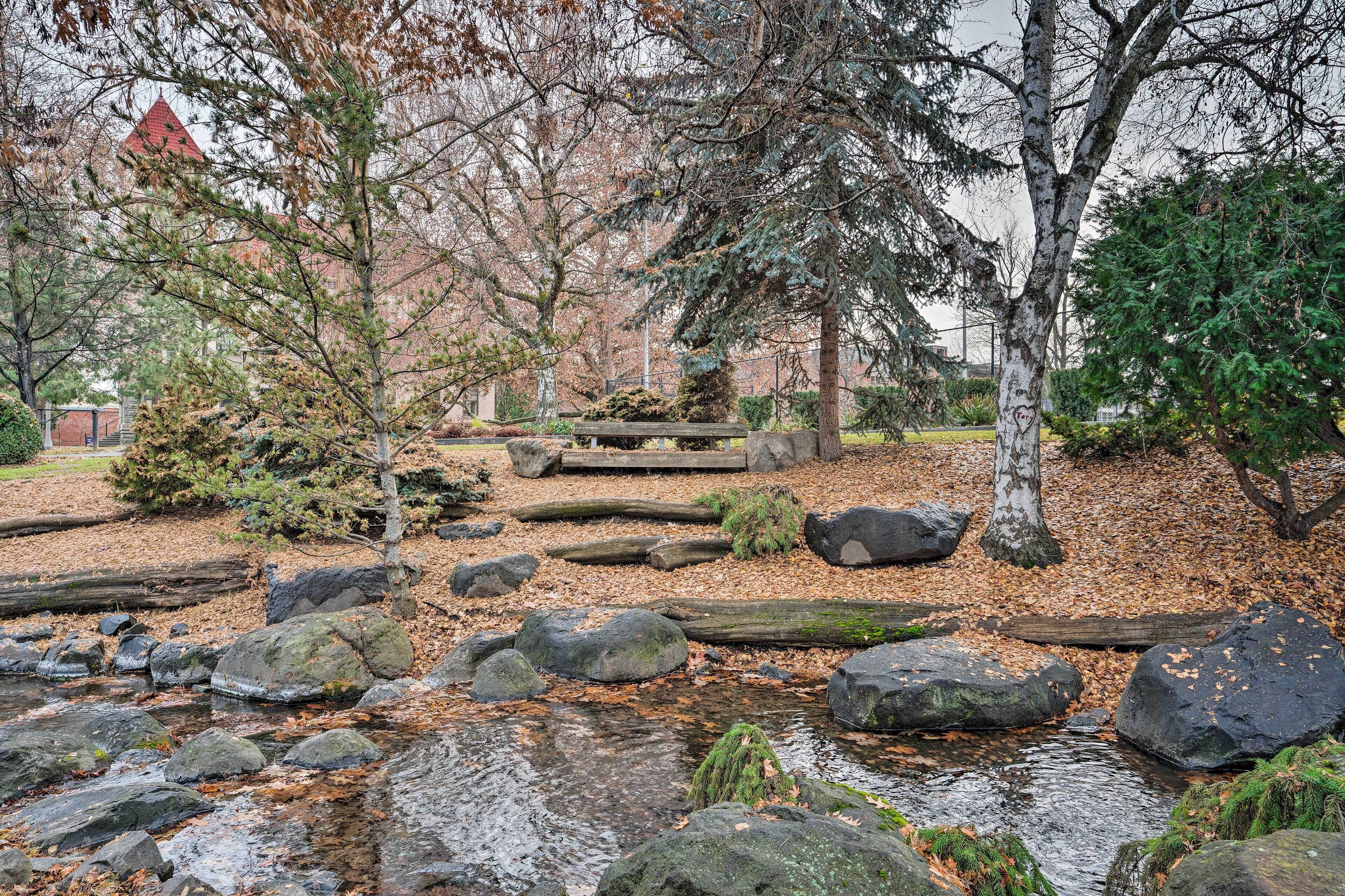 A serene park with a stone bench, large rocks, and a small stream.