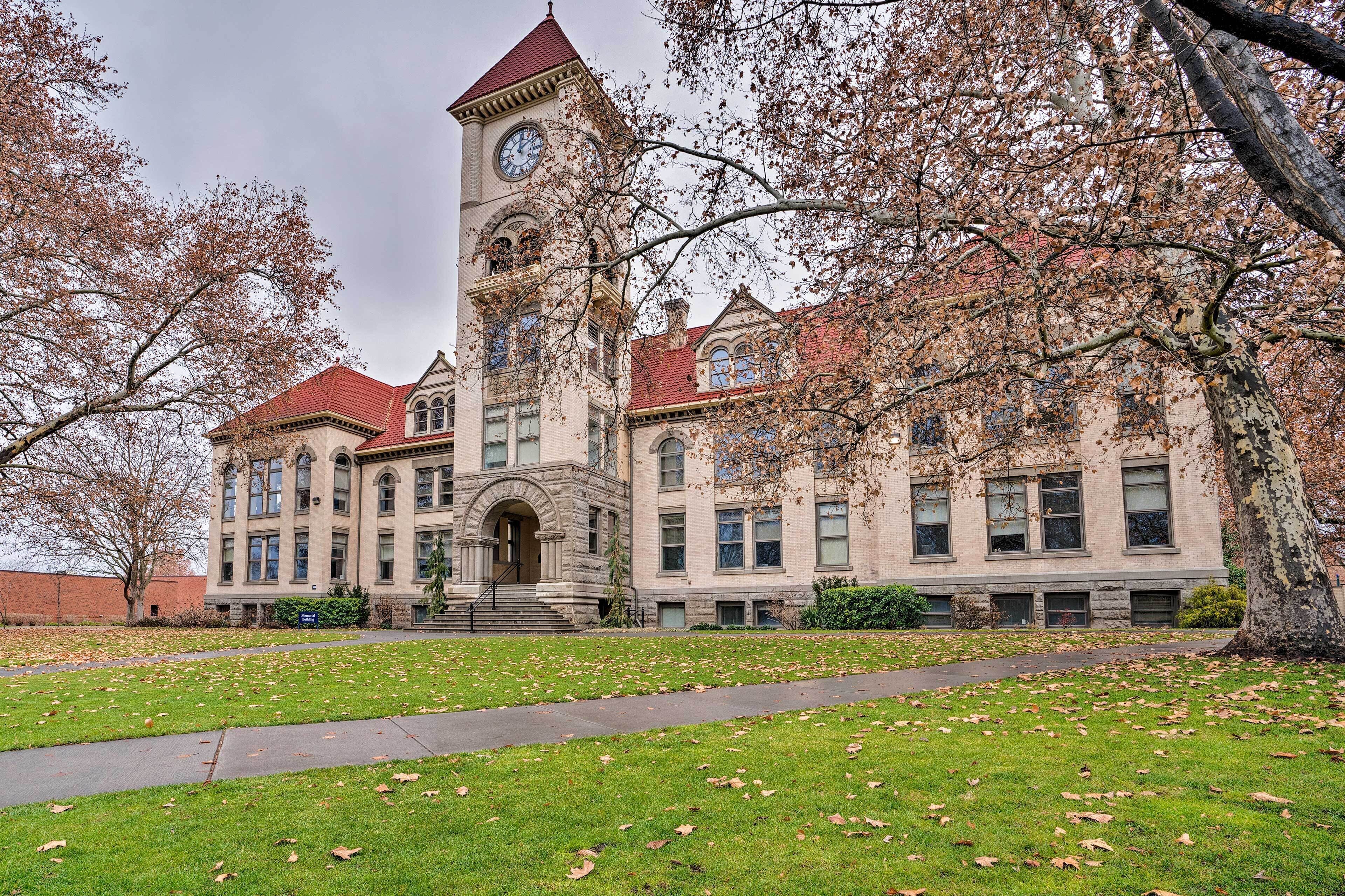 A historic building with a prominent clock tower, large windows, and a well-maintained lawn.
