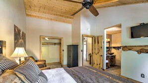 Ein Schlafzimmer mit einem Bett, einem Deckenventilator, einem an der Wand montierten Fernseher und einer Holztür.