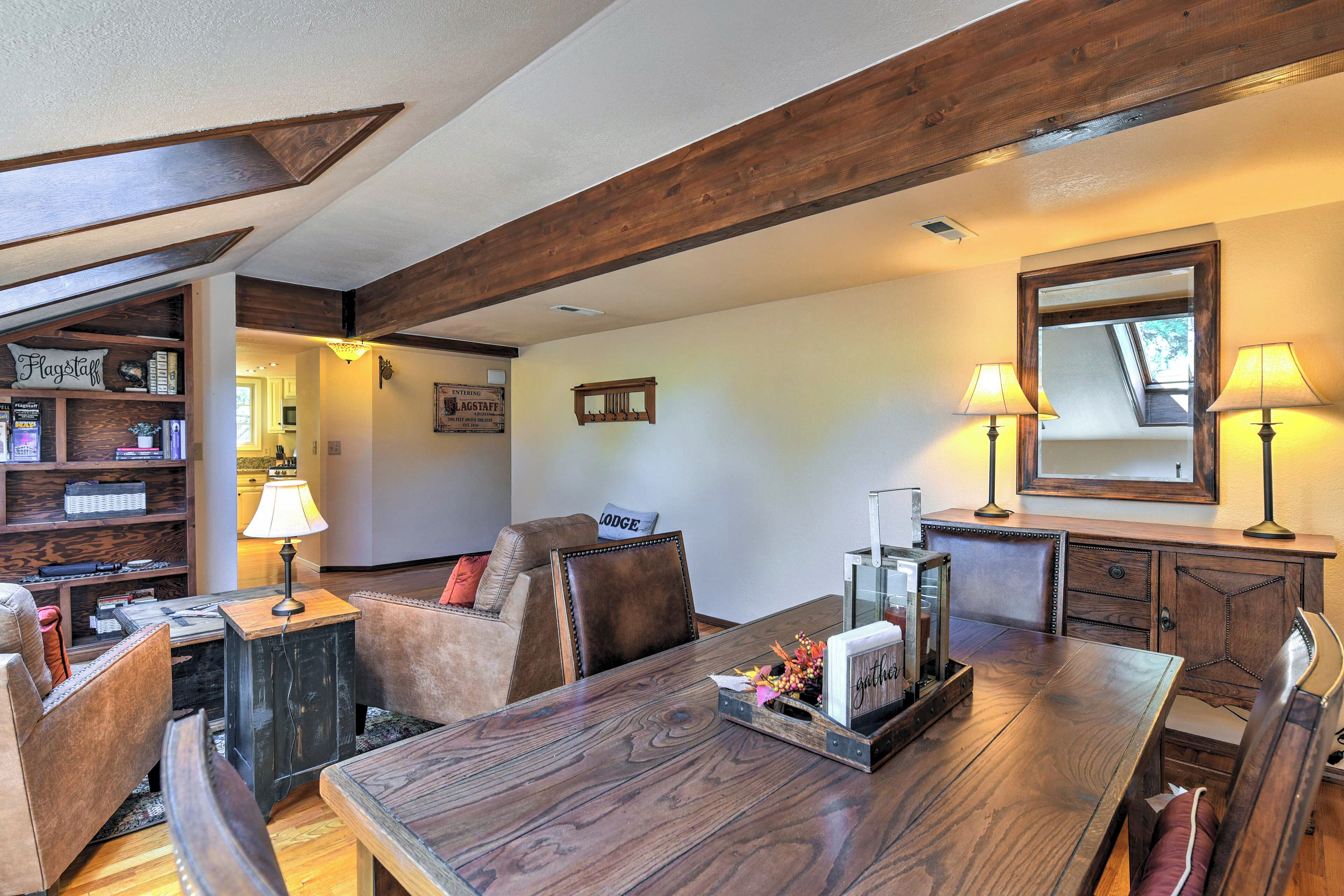 A dining area with a wooden table, chairs, and a bookshelf with various items.