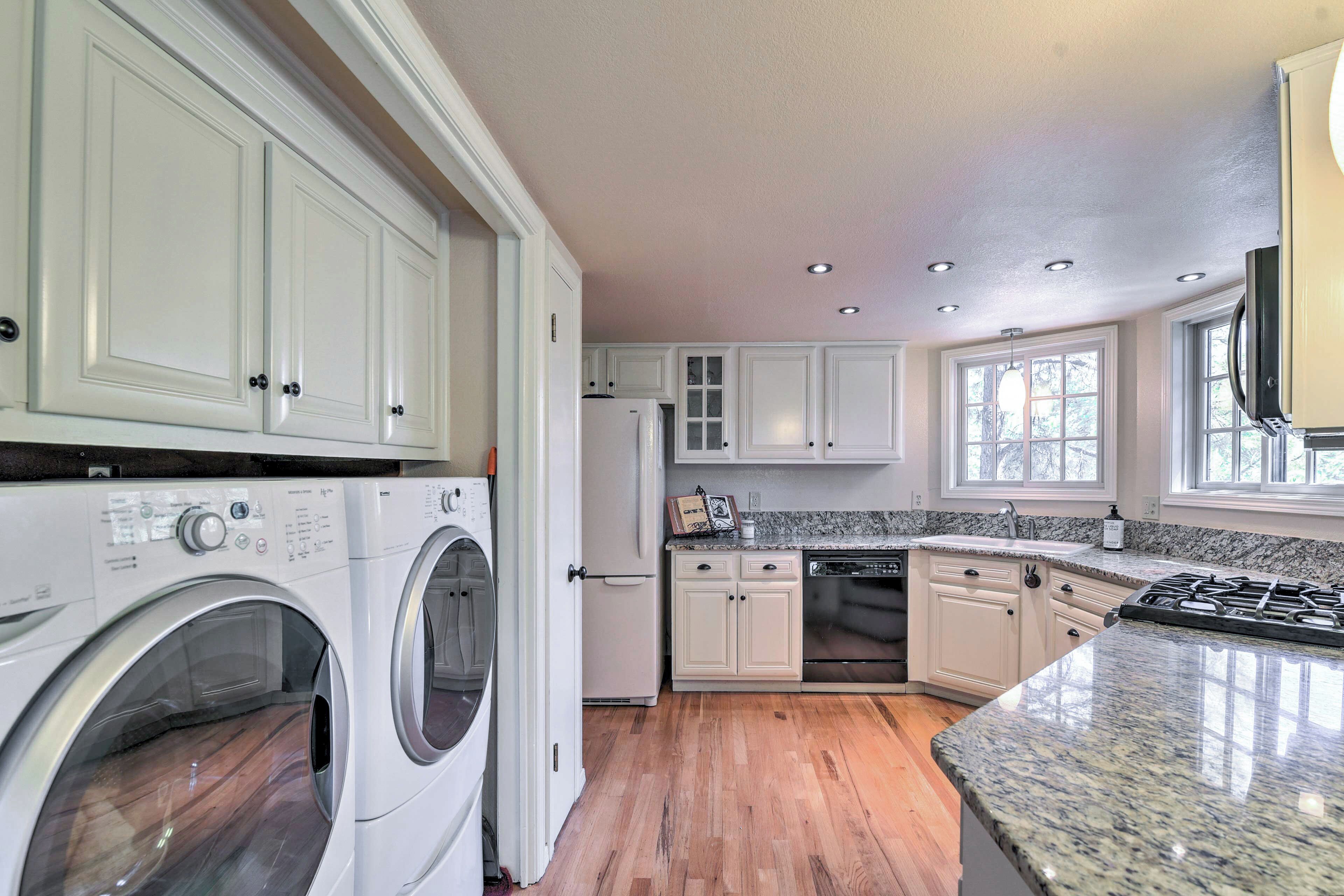 A kitchen with white cabinets, a built-in washer and dryer, a stove, and a large window providing natural light.
