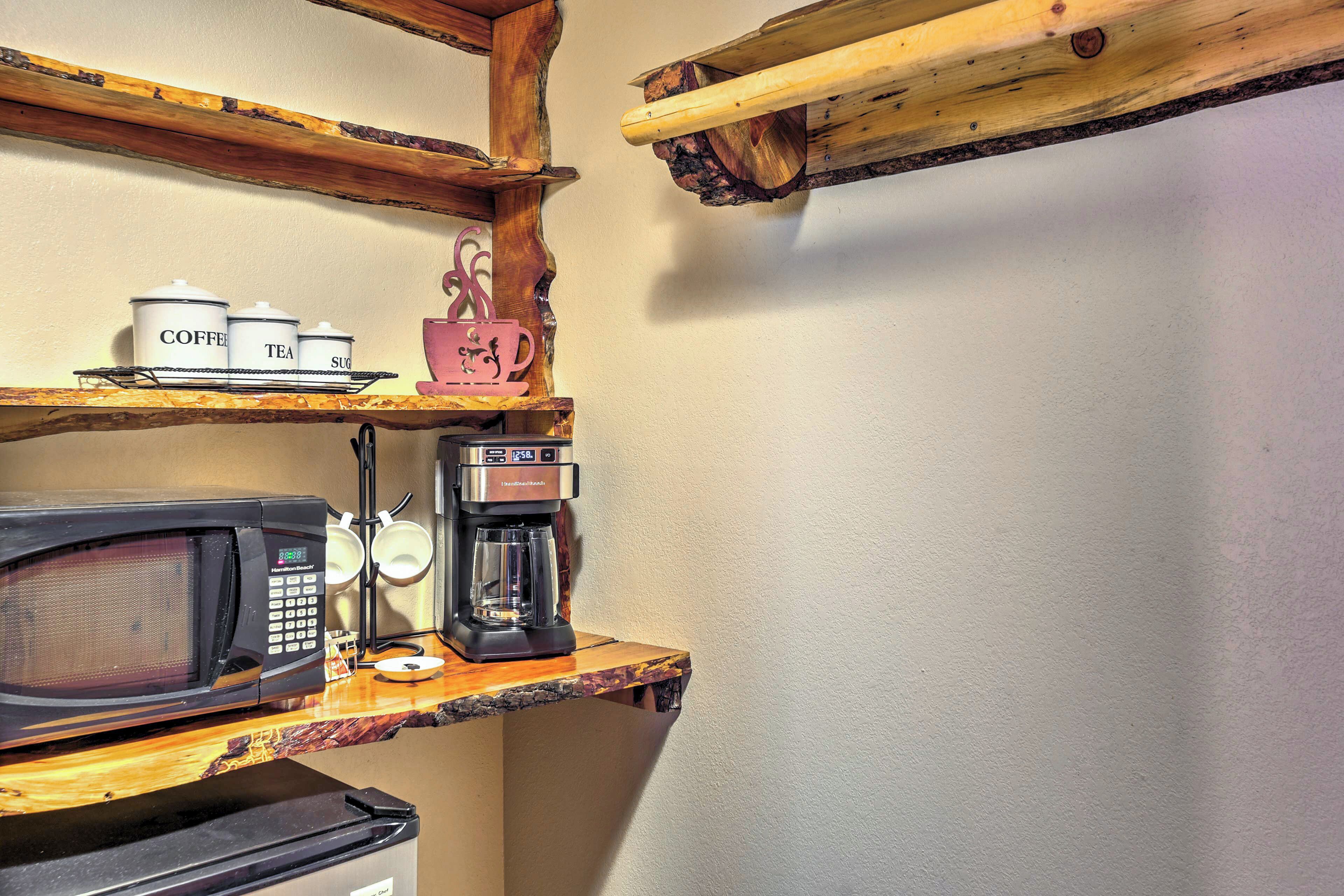 A kitchen with a microwave, coffee maker, and storage containers labeled coffee, tea, and sugar.