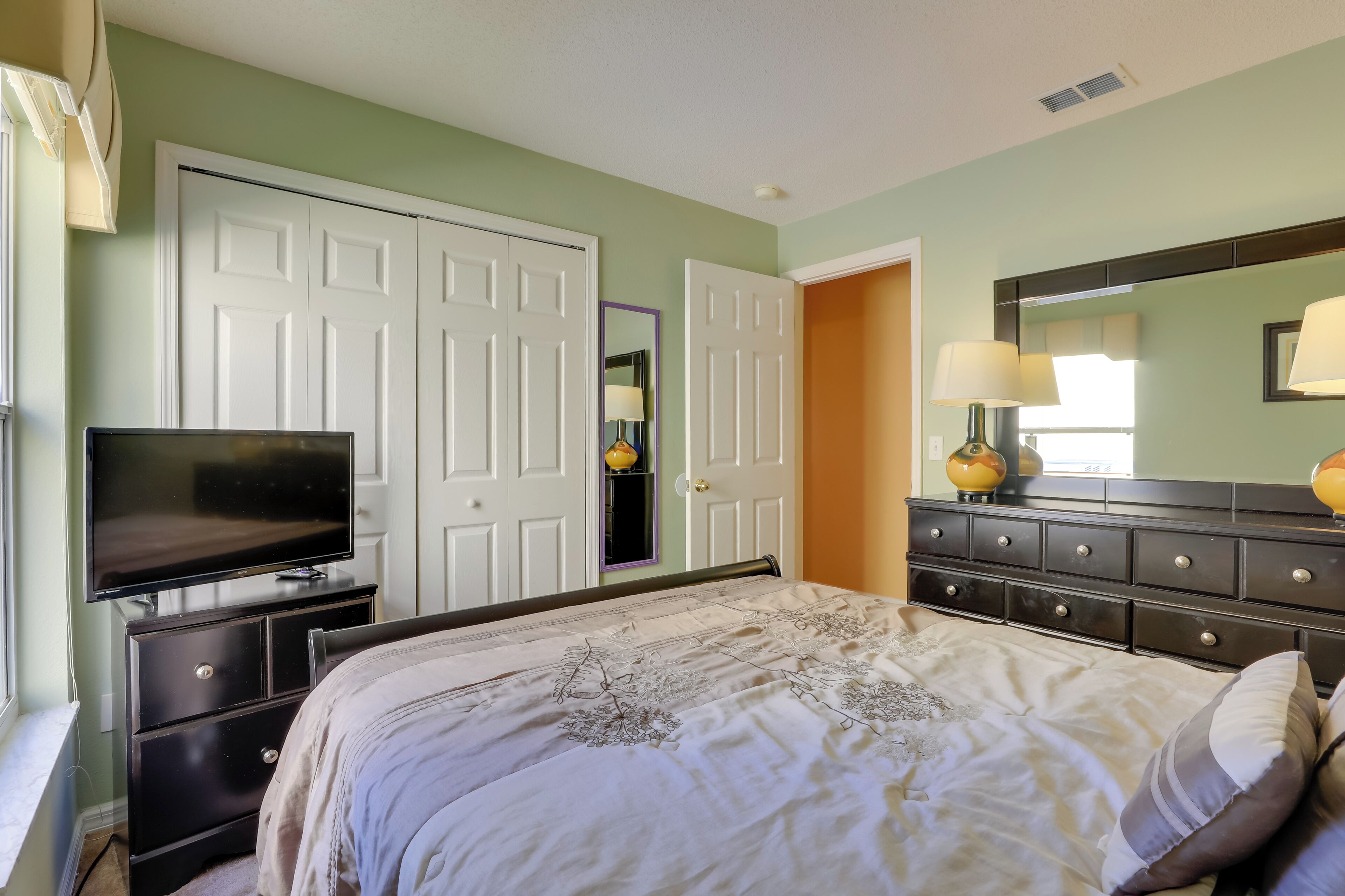 A bedroom with a bed, dresser, television, and a door leading to another room.