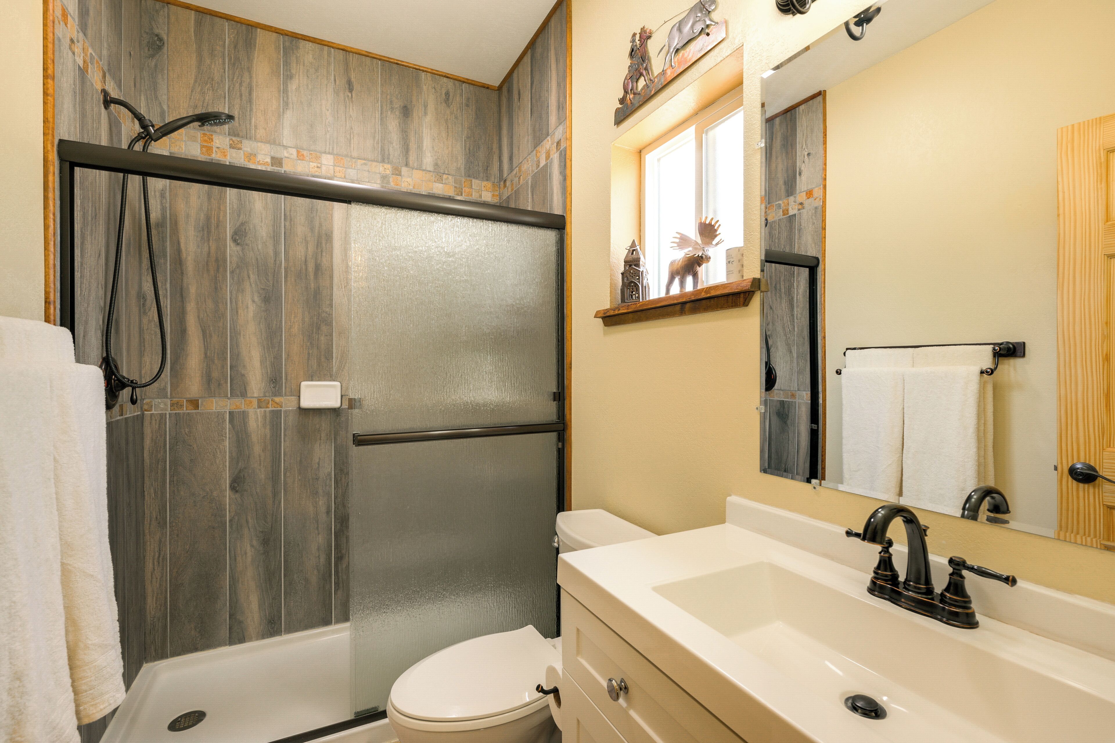 A bathroom with a shower, toilet, sink, and mirror.