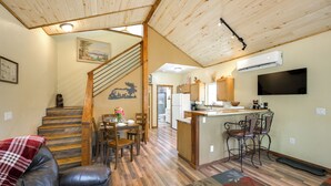 A spacious living area with a wooden staircase, a dining table with chairs, a kitchen area with a bar, and a flat-screen TV mounted on the wall. - 'cabin at the Little Ranch' w/ Hiking On-site! (Bayfield)