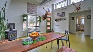 A dining area with a wooden table, chairs, a bowl of fruit, a mounted deer head, and a fireplace.