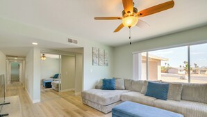 A spacious living room with a large sectional sofa, a ceiling fan, and a large window offering a view of the outside. - Location! Home w/ Pool 1 Min to Mcculloch Blvd (Lake Havasu City)