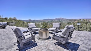 Eine Dachterrasse mit vier grau gepolsterten Stühlen und einem Metalltisch, mit Blick auf eine gebirgige Landschaft.