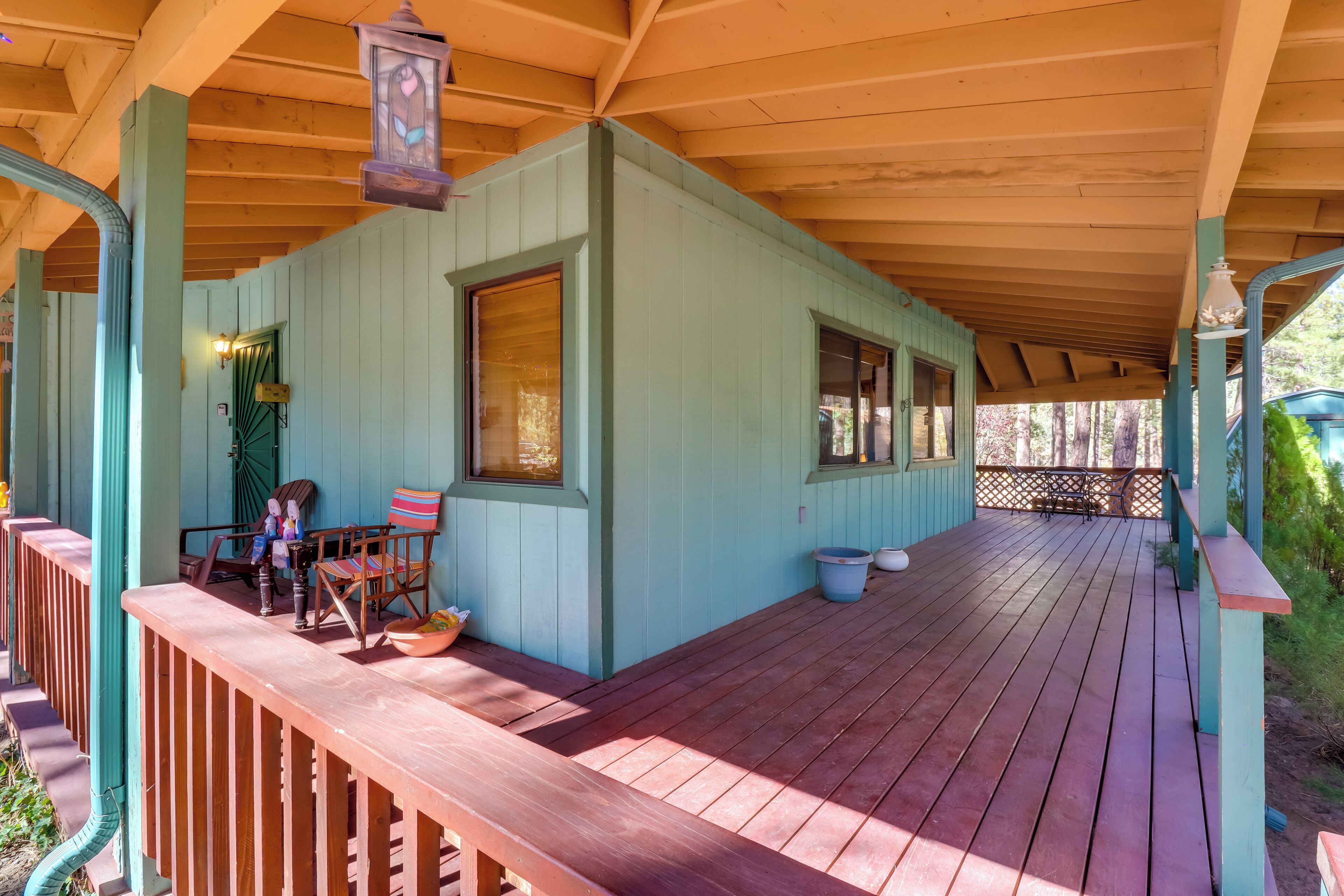 A covered wooden deck with a railing, a bench, and a table.