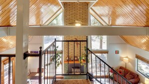 A multi-level wooden interior with a staircase, a fireplace, and a seating area with a sofa and a lamp. - Relax Fireside: Rustic Gem 2 Mi to Rainbow Lake! (Lakeside)