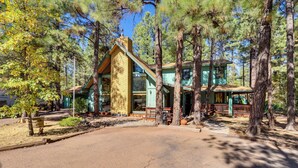 A lodge with a stone chimney, wooden deck, and a large window overlooking the forest. - Relax Fireside: Rustic Gem 2 Mi to Rainbow Lake! (Lakeside)
