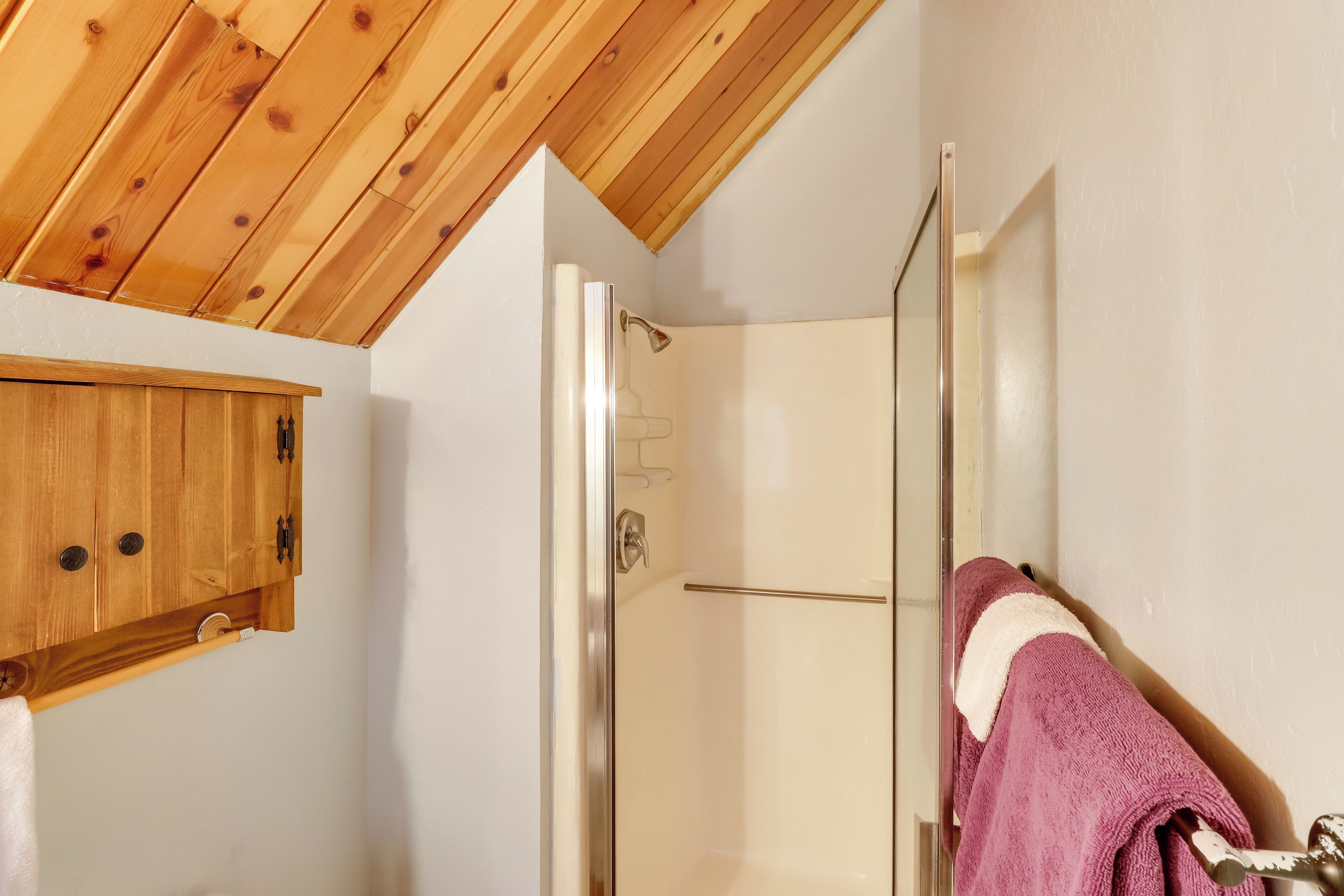 A bathroom with a wooden ceiling, a glass shower door, and a towel rack with a purple towel.