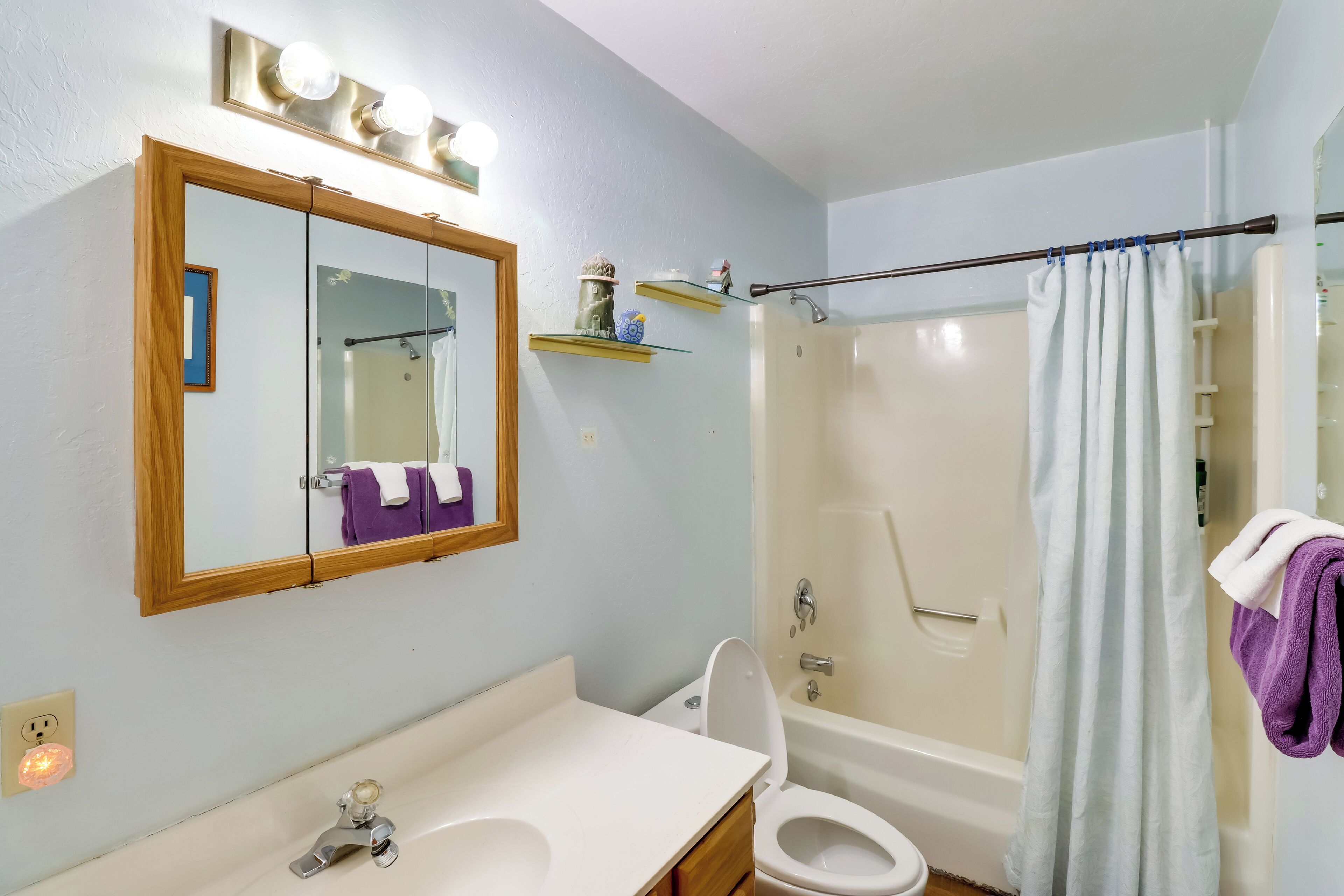 A bathroom with a white sink, a toilet, a bathtub, and a shower. There is a mirror with a wooden frame and a shelf above it.