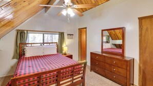 A bedroom with a wooden ceiling, a bed with a checkered bedspread, a dresser, a mirror, and a ceiling fan. - Relax Fireside: Rustic Gem 2 Mi to Rainbow Lake! (Lakeside)