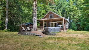 Un chalet rustique doté d’une véranda, d’un petit abri de jardin et d’un chemin de pierre menant à l’entrée.